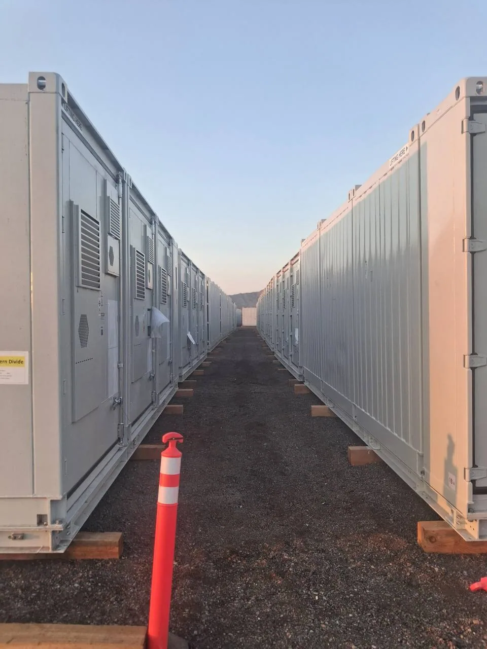 Service corridor running between two rows of delivered battery energy storage containers at dusk