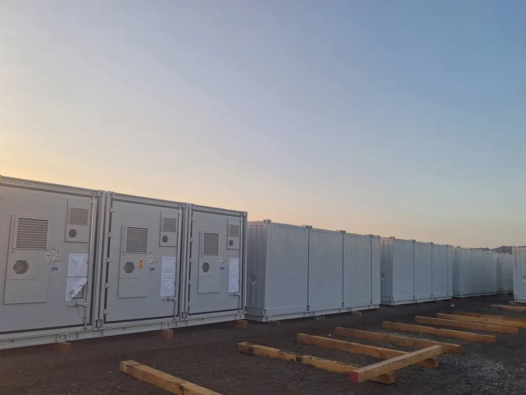 Battery storage containers staged at dusk with empty timber sleepers pre-set for the next delivery