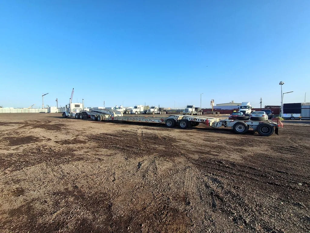 Extendable lowboy and removable-gooseneck trailers with heavy-haul tractors staged at a project laydown yard