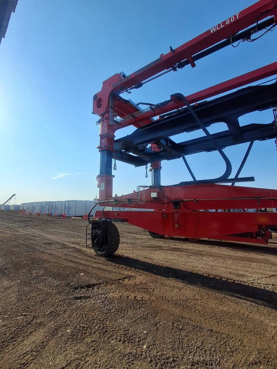 Low-angle view of a straddle carrier lifting boom stamped WLL 60T against a clear sky