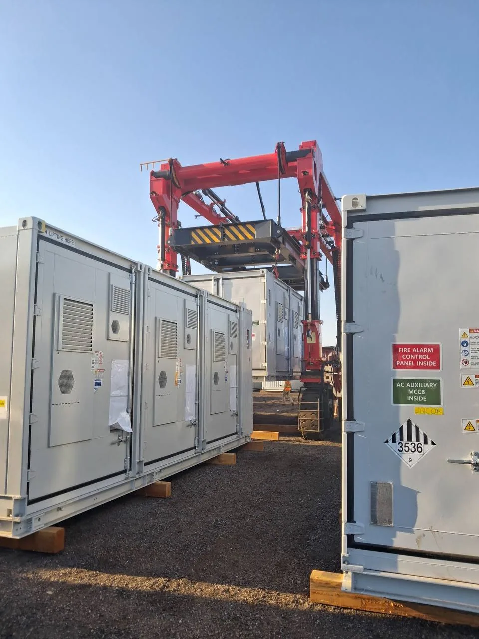Straddle carrier manoeuvring between placarded battery containers during final placement